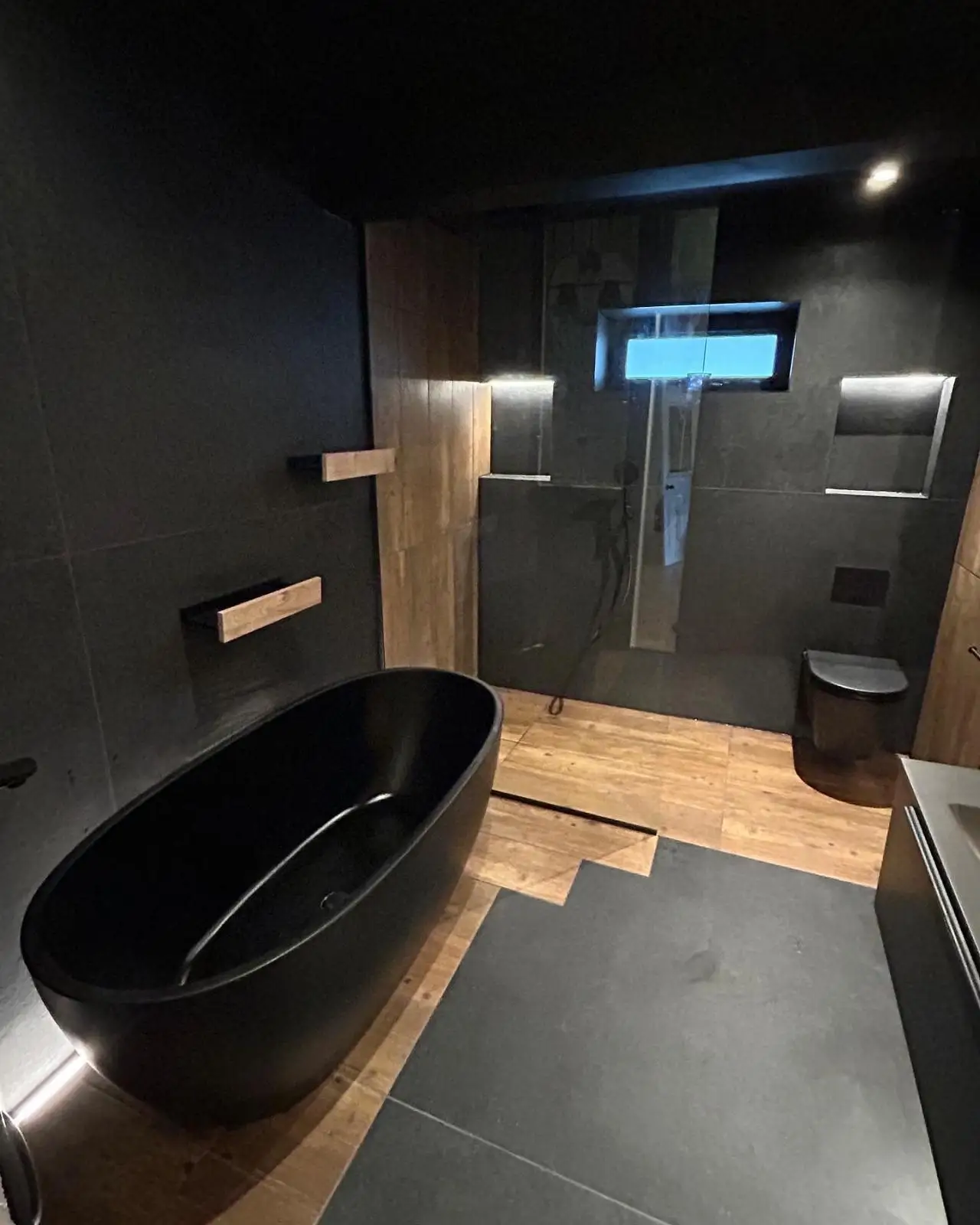 Reforma de baño con bañera exenta negra, paredes oscuras y suelo de madera en Madrid