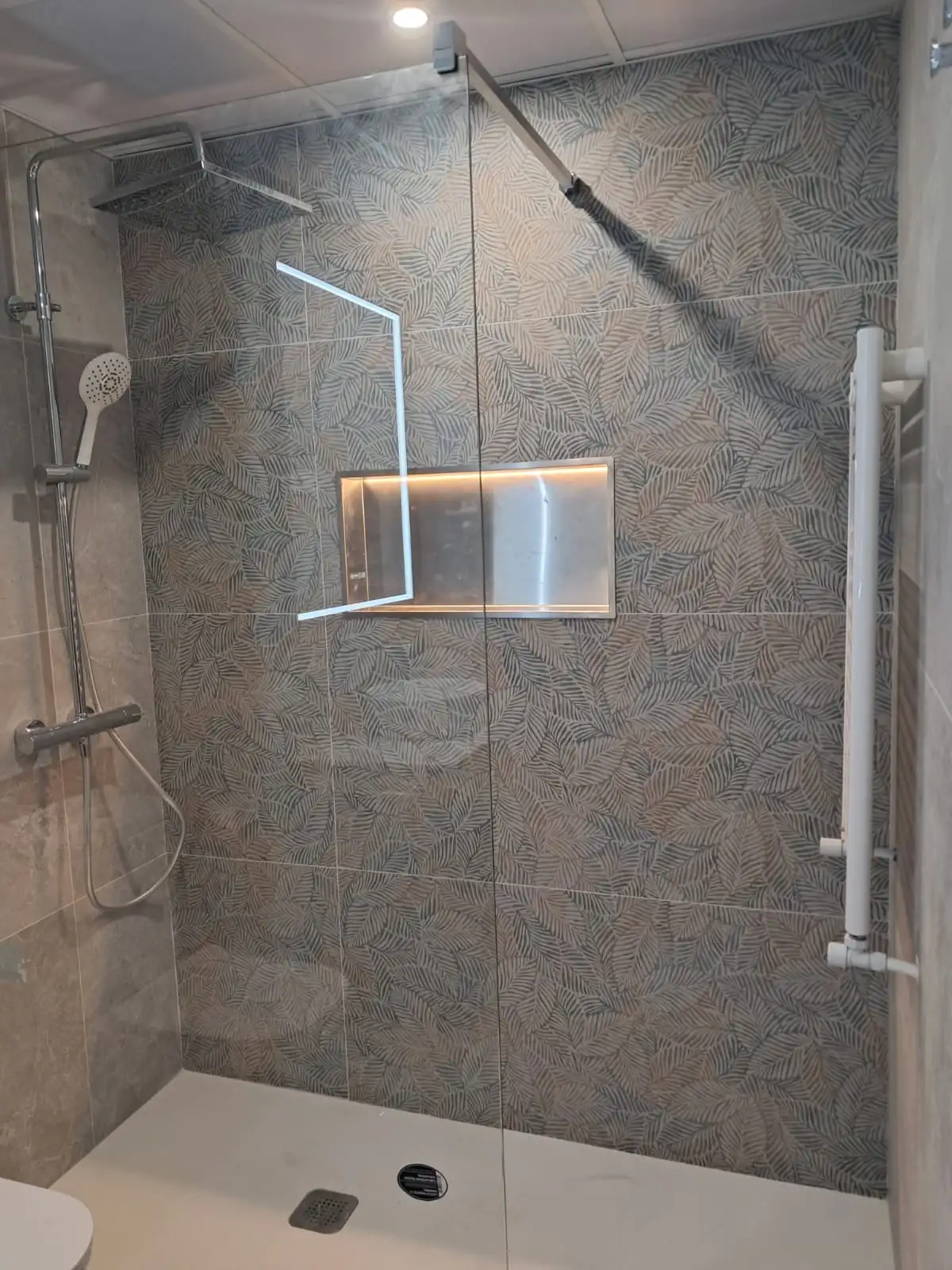 Reforma de baño con ducha de azulejos decorativos de hojas y hornacina iluminada en Madrid