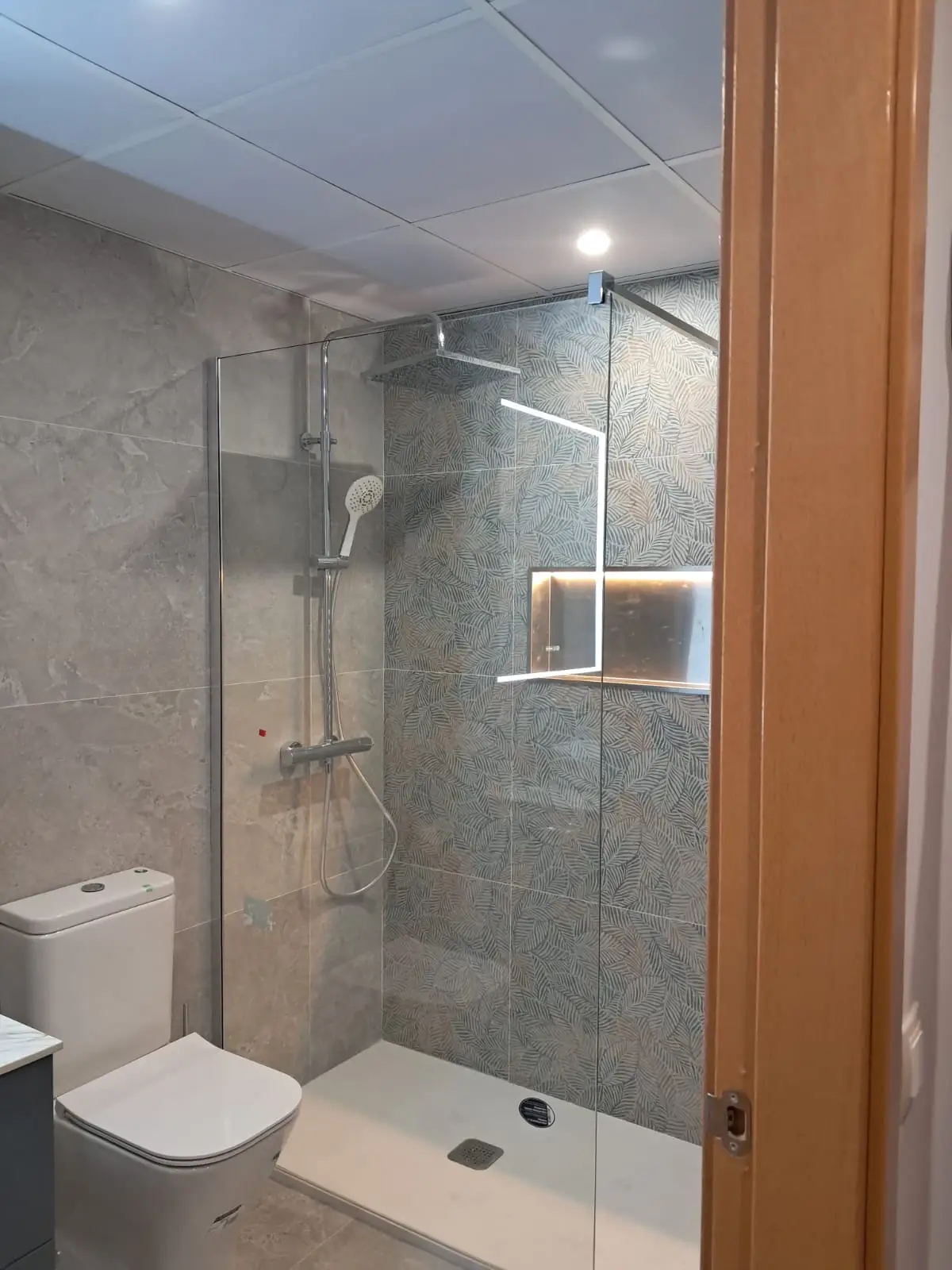 Reforma de baño con plato de ducha blanco, mampara de cristal y azulejos decorativos de hojas en Madrid