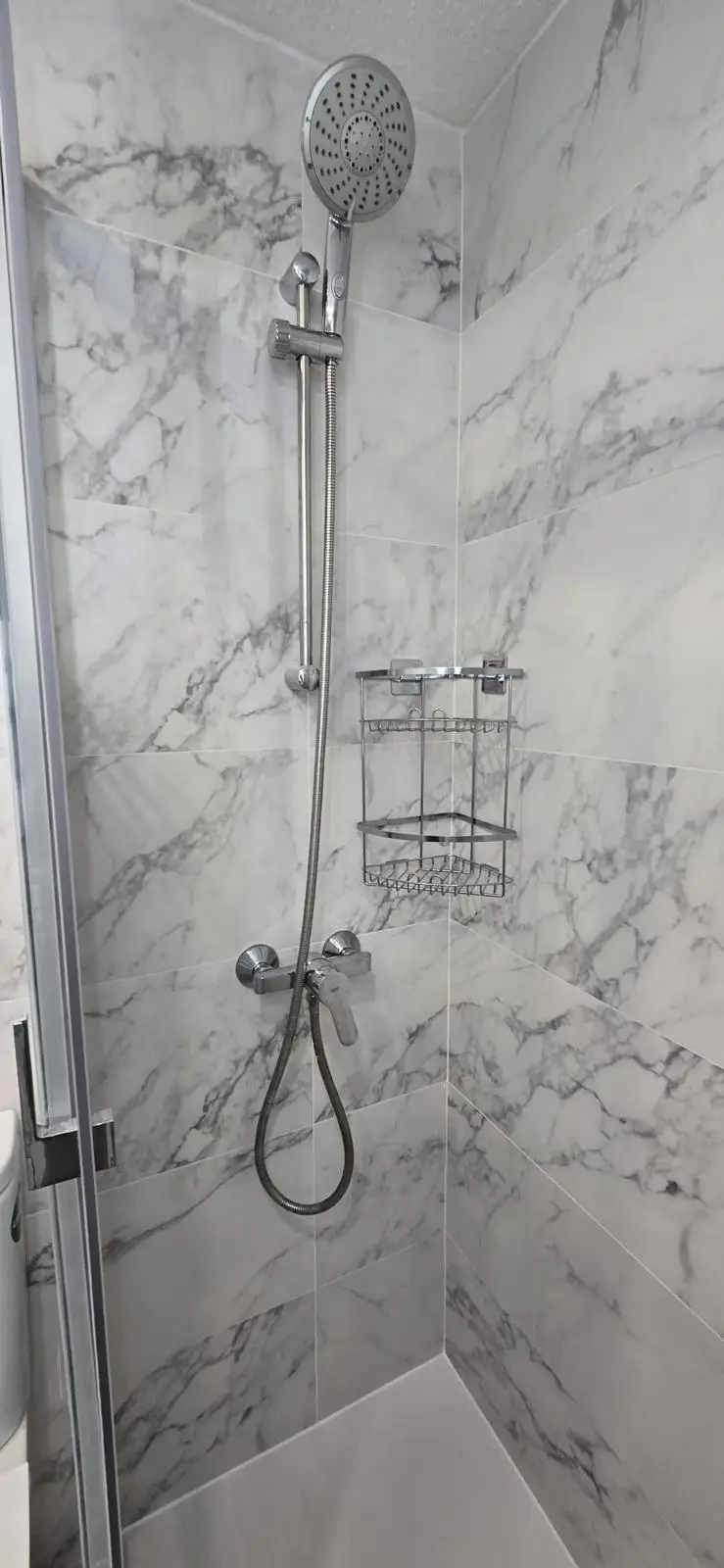 Reforma de baño con revestimiento de mármol blanco y grifería cromada en Madrid