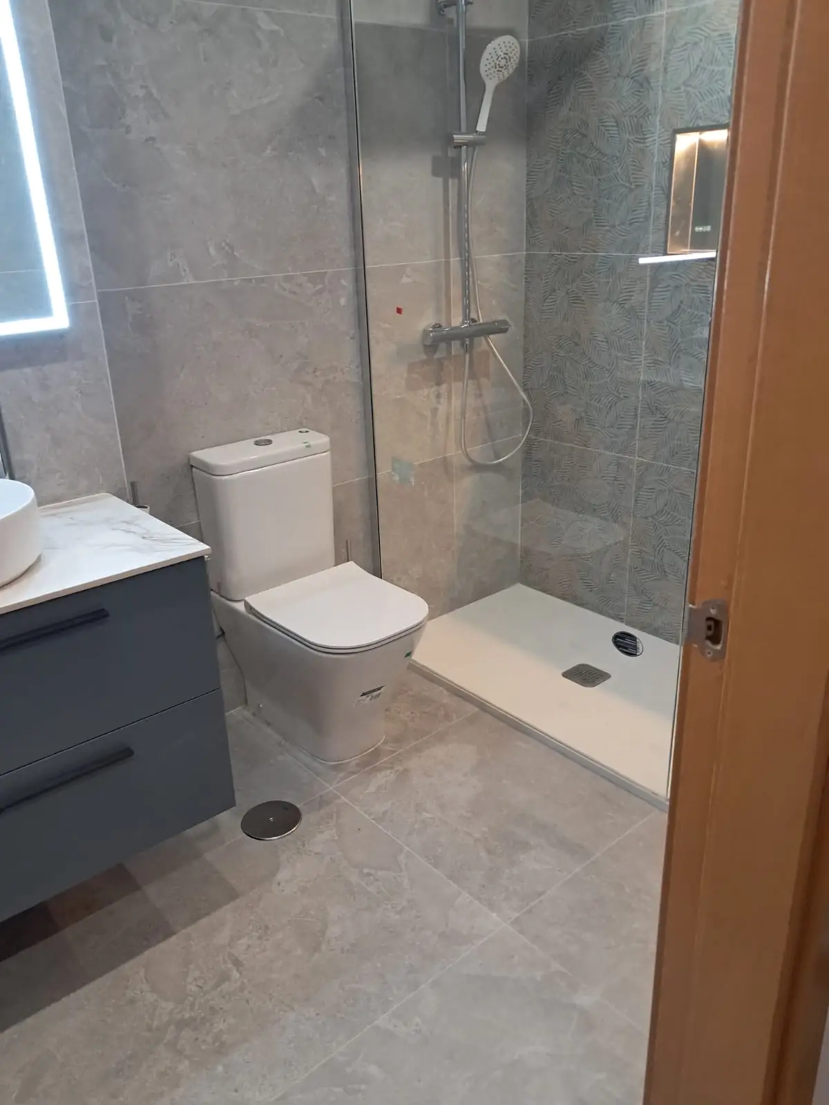 Reforma de baño con ducha de azulejos decorativos de hojas y hornacina iluminada en Madrid