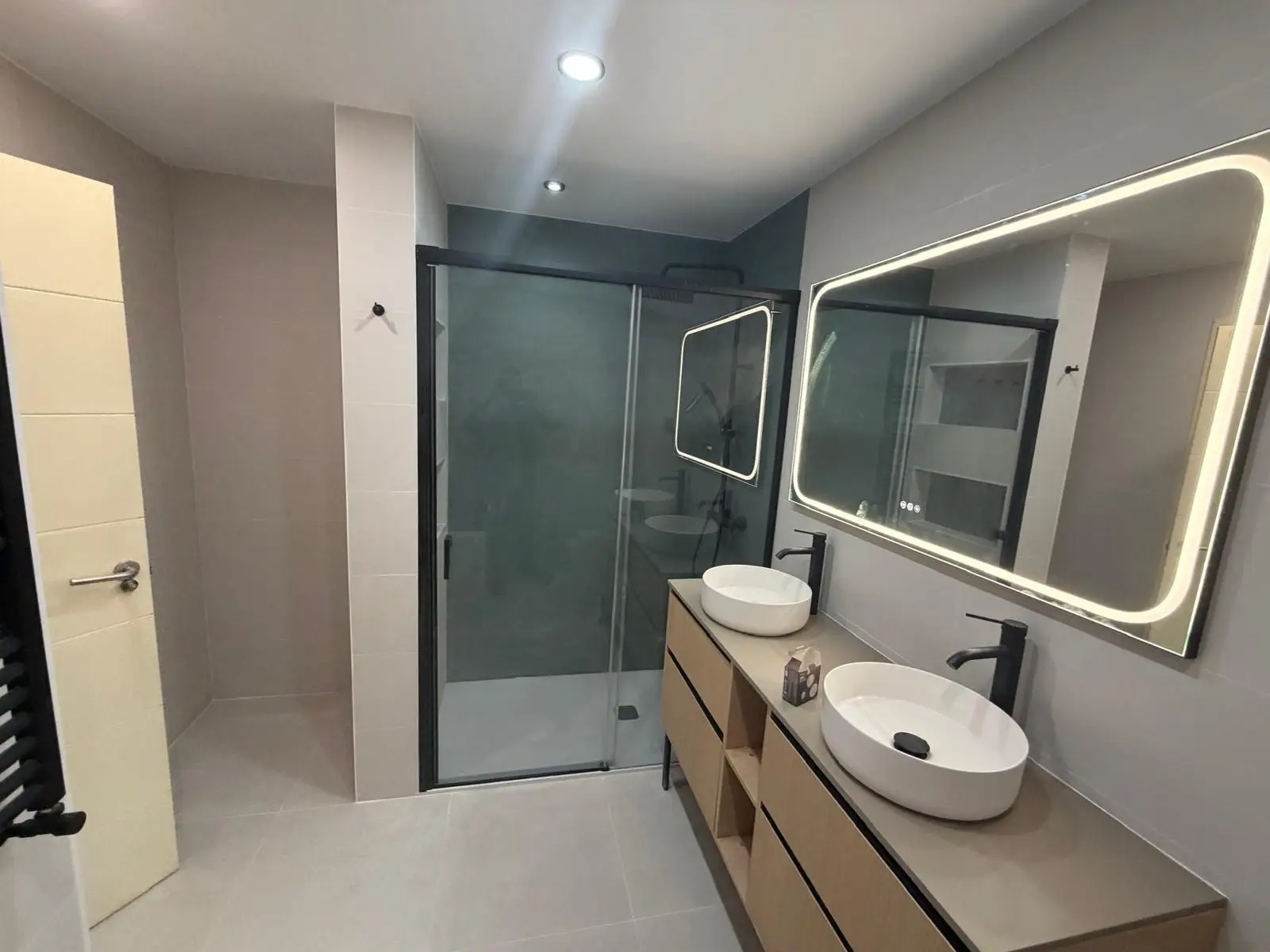 Reforma de baño con mueble de madera, lavabo doble sobre encimera y espejo retroiluminado en Madrid
