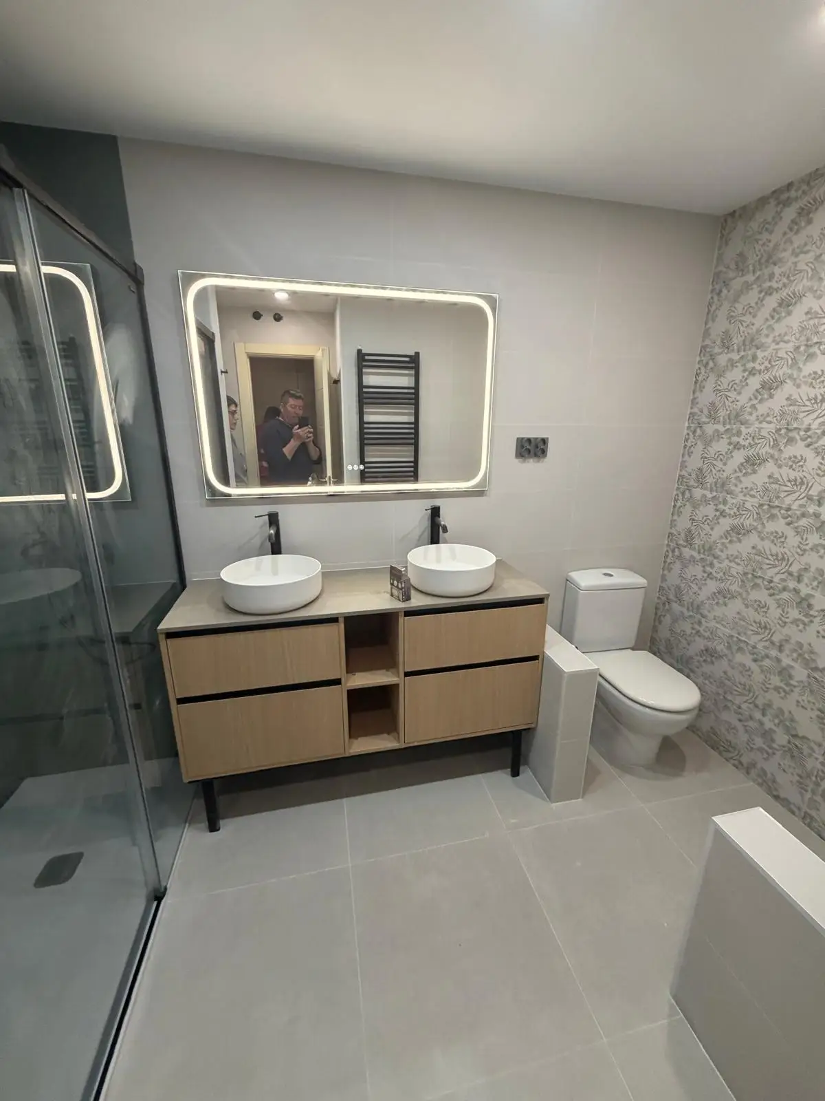 Reforma de baño con mueble de madera, lavabo doble sobre encimera y espejo retroiluminado en Madrid