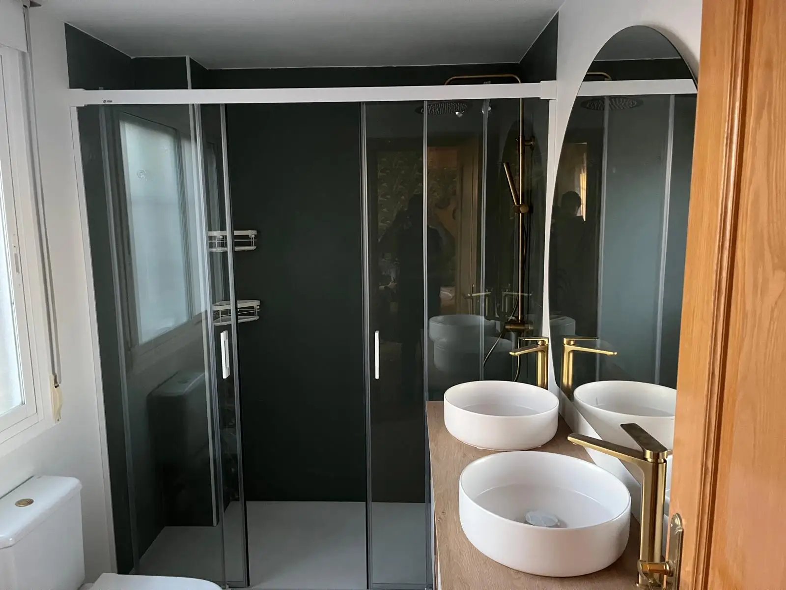 Reforma de baño con lavabos de sobremesa blancos, grifería dorada y mampara oscura en Madrid