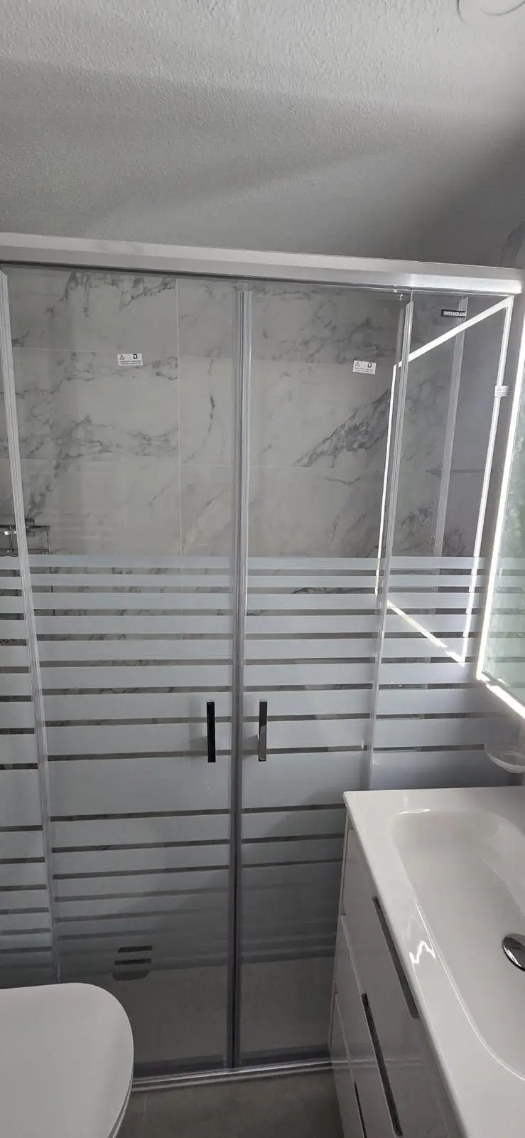 Reforma de baño con mampara serigrafiada y revestimiento cerámico efecto mármol en Madrid