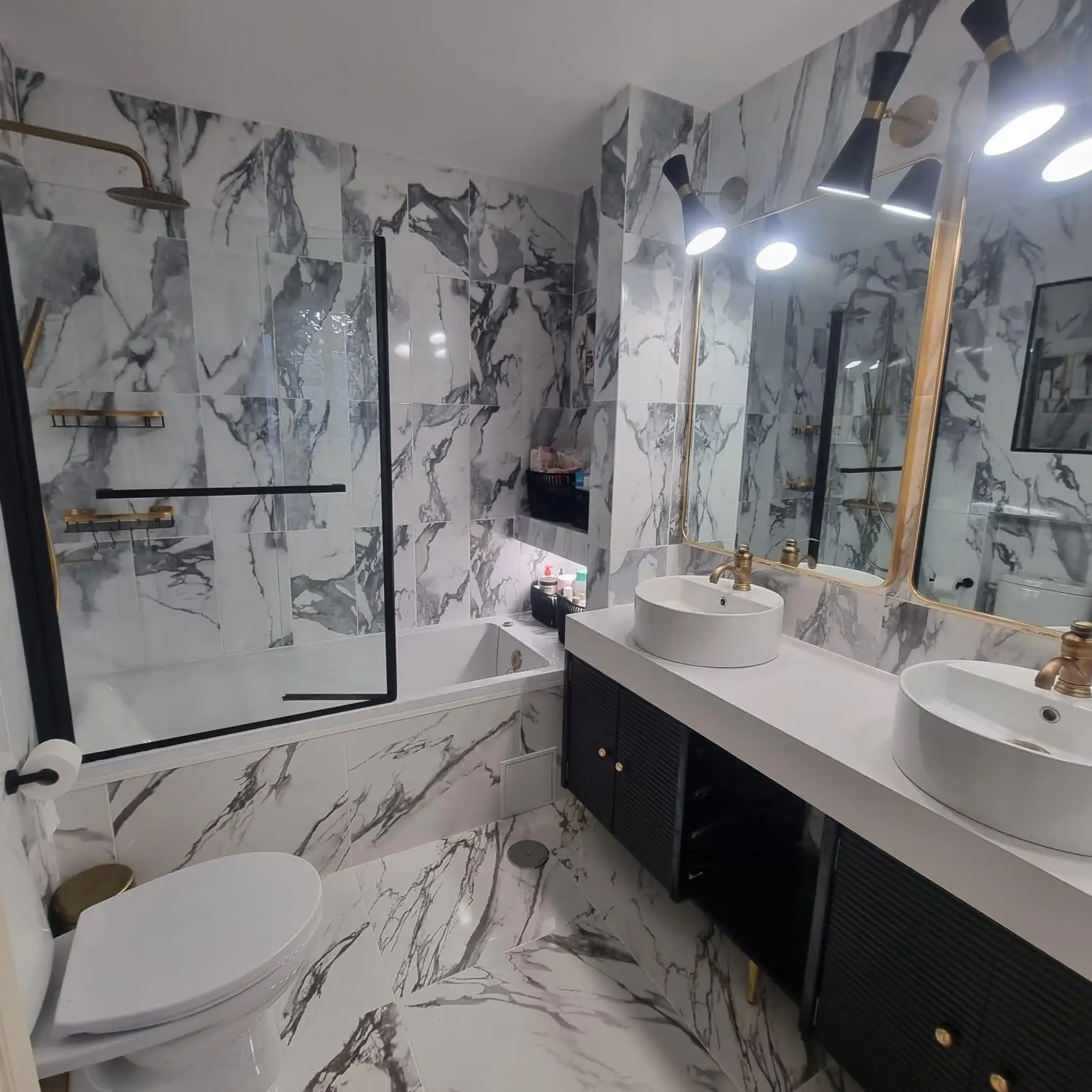 Reforma de baño con revestimiento de mármol blanco, grifería dorada y lavabo doble en Madrid