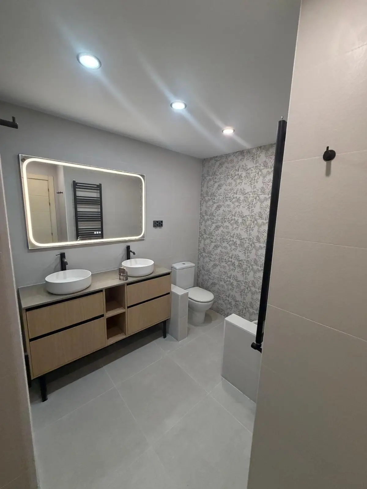 Reforma de baño con mueble de madera, lavabos sobre encimera y espejo retroiluminado en Madrid