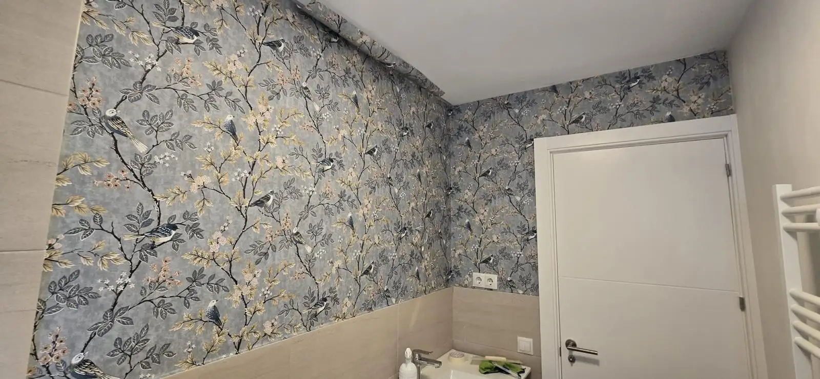 Reforma de baño con papel pintado de motivos florales y pájaros sobre zócalo cerámico en Madrid