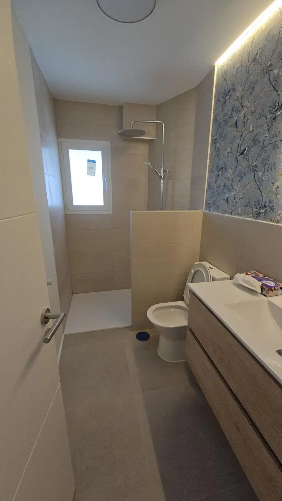 Reforma de baño con papel pintado de motivos florales y pájaros sobre zócalo cerámico en Madrid