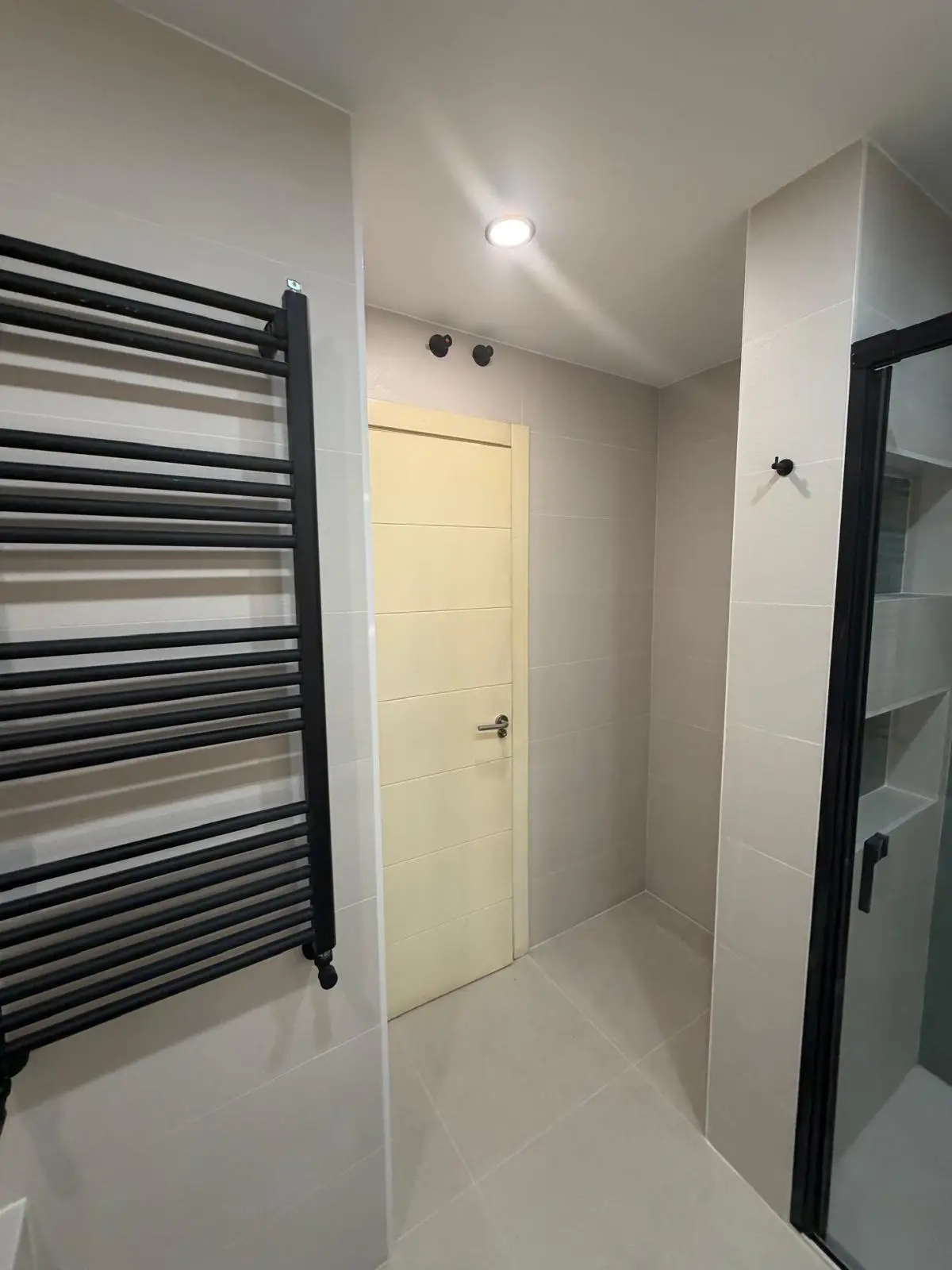 Reforma de baño con radiador toallero negro mate y paredes alicatadas en tonos grises en Madrid